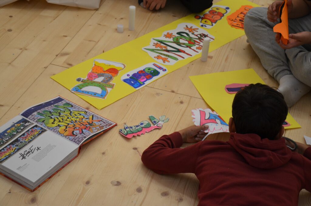 Stock Bild: Kinder liegen auf dem Boden, malen und kleben Kollagen.